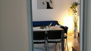 A dining area with a table and chairs, a blue sofa, a wall-mounted painting, and a potted plant.