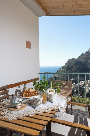 Un balcón con una mesa de madera dispuesta para el desayuno, con vista al mar.