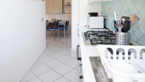 A kitchen with white cabinets, a gas stove, and a microwave. There is a dining area with a table and chairs visible through an archway.