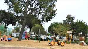 Un terrain de jeux doté de diverses installations, notamment un toboggan et des structures d’escalade, entouré d’arbres et d’une zone sablonneuse.