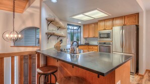 Una cocina moderna con armarios de madera, un refrigerador de acero inoxidable, una isla grande con taburetes y una lámpara colgante.