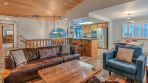 Amplia sala de estar con techo de madera, un sofá de cuero, un sillón azul y una cocina al fondo.
