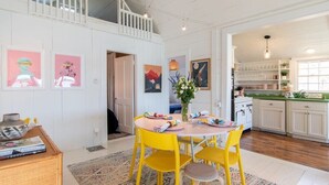 A dining area with a round table and yellow chairs, a white ceiling, and a kitchen with white cabinets and a green countertop.