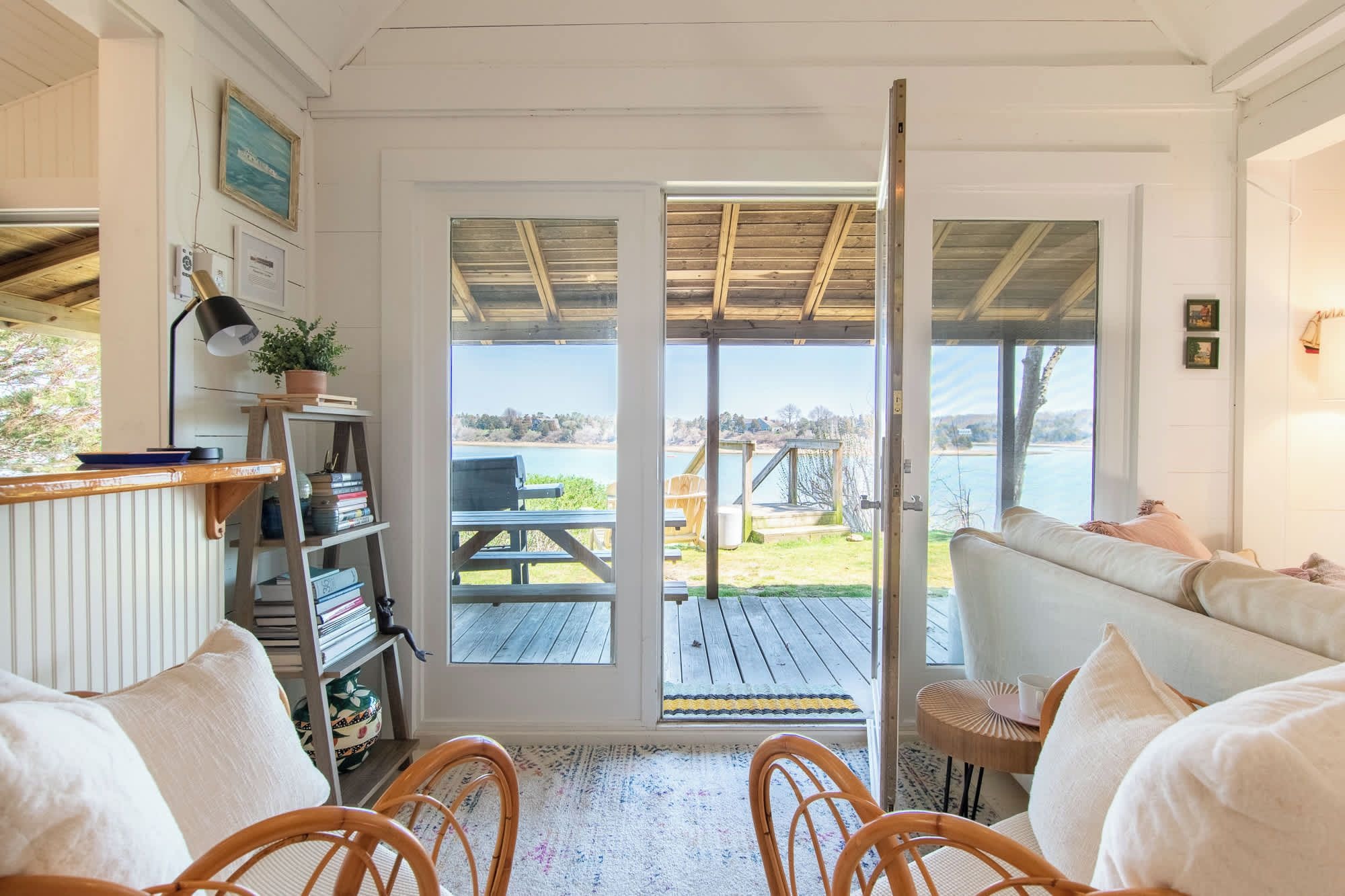 A room with a view of a lake, a wooden ceiling, a sofa, a bookshelf, and a dining area.
