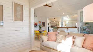 A cozy living room with a beige sofa, a round coffee table, and a dining area with yellow chairs.