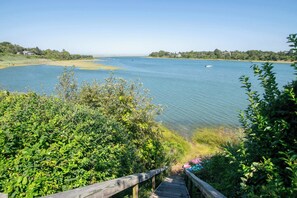 A wooden boardwalk leading to a lake with clear water and a view of distant houses on the shore. - Seaside Retreat w/ Private Beach Landing! (Eastham)
