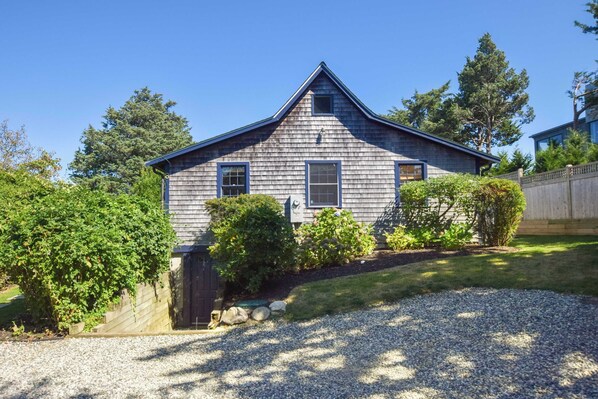 A single-story house with a gabled roof, surrounded by a well-maintained lawn and various shrubs. - Seaside Retreat w/ Private Beach Landing! (Eastham)
