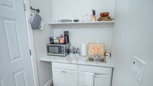Eine kleine Küche mit weißen Schränken, einer Mikrowelle, einer Kaffeemaschine und einem Spülbecken.