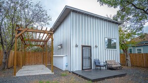 Ein kleines, eingeschossiges Gebäude mit Metallfassade, einer Holzpergola und einer kleinen Terrasse mit zwei Stühlen.