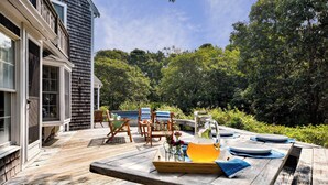 A wooden deck with outdoor furniture, a table set for a meal, and a house in the background. - Walk to Water Hot Tub & Game Room! (Eastham)