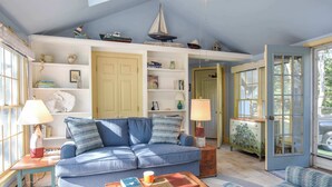 A cozy living room with a blue sofa, wooden coffee table, and a bookshelf filled with books and decorative items. - Walk to Water Hot Tub & Game Room! (Eastham)