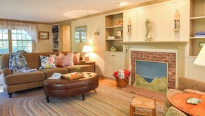 A cozy living room with a fireplace, a sofa, a coffee table, and a bookshelf. - Walk to Water Hot Tub & Game Room! (Eastham)