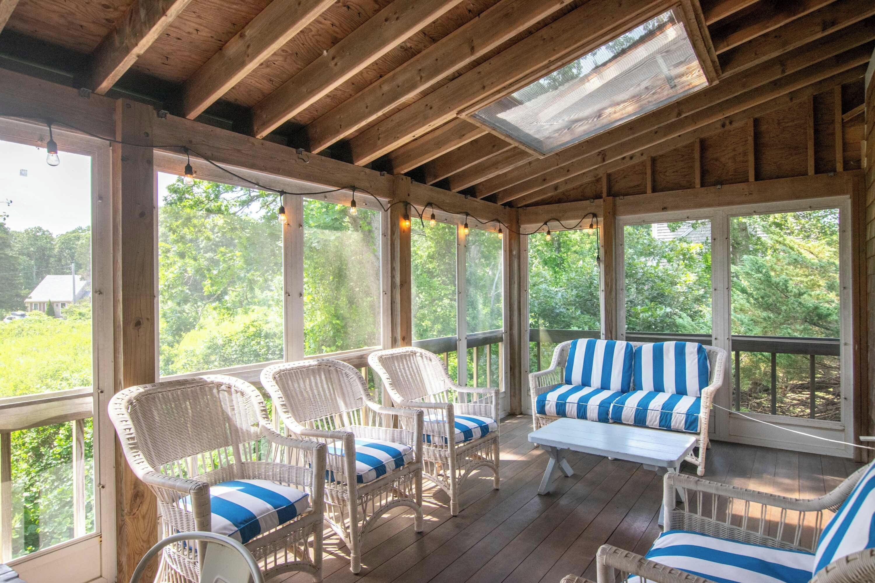 A covered porch with wicker furniture and a view of greenery.