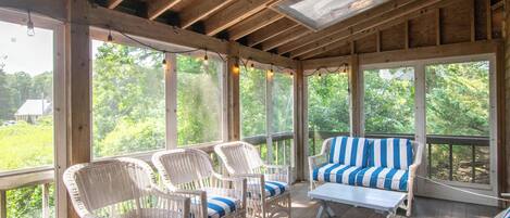 A covered porch with wicker furniture and a view of greenery.