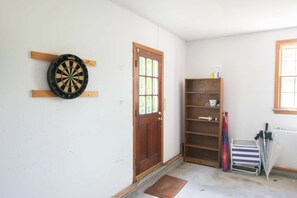 Una habitación con dardos, una puerta de madera, un estante con objetos y una ventana.