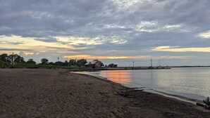 Ranta, jossa on puinen rakennelma, laituri, joka ulottuu tyyniin veteen, ja auringonlasku taustalla.