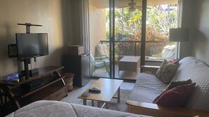 A hotel room with a bed, a TV, a small table, a sofa, and a balcony with chairs and a table. - Relax and Rejuvenate in the Heart of Kona. Minutes walk to town! (Kailua-Kona)