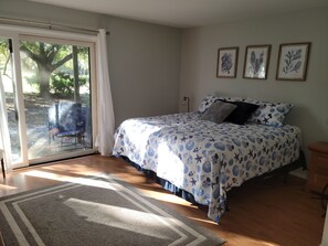 A bedroom with a bed, a sliding glass door leading to a patio, and three framed botanical prints on the wall.