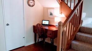 Une pièce avec un bureau en bois, une chaise, un ordinateur portable, une horloge et un escalier.