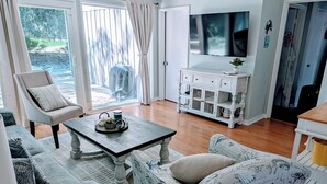 Un salon comprenant un canapé, un fauteuil, une table basse, un téléviseur et un meuble.