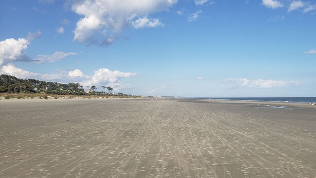 Une vaste plage de sable, parsemée d’empreintes, sous un ciel dégagé.