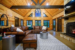 Relax in this cozy cabin with a stone fireplace, leather sofa, and large windows offering forest views.