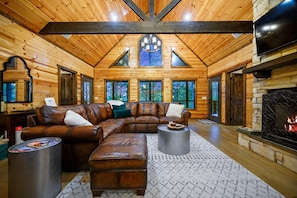 Relax in this cozy cabin with a stone fireplace, leather sofa, and large windows offering forest views.