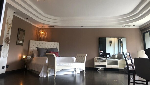 A modern bedroom with a large bed, a chandelier, a mirror, and a dresser. - Woodlands San Rafael Heredia , Costa Rica (Montecito)