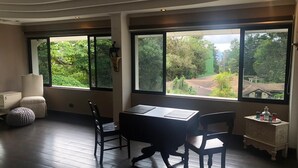 A room with a desk, two chairs, a small cabinet, and large windows offering a view of greenery. - Woodlands San Rafael Heredia , Costa Rica (Montecito)