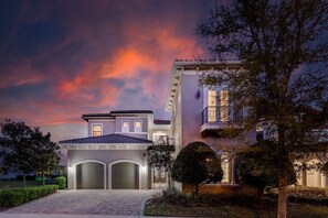 Stucco-clad building with a central entrance and arched doorways, set amidst well-manicured landscaping.