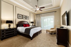 A hotel room with a large bed, a desk, a chair, a television, and a ceiling fan. - The Oasis at Reunion | 8 Bed, 8 Bath Luxury Villa, Game Room, Private Pool & Spa (Kissimmee)