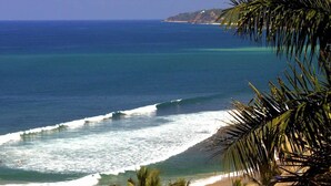 A beach with waves, palm trees, and a distant island.