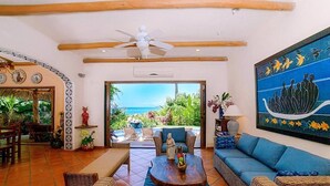 A spacious living area with a ceiling fan, a large painting, and a view of the ocean.