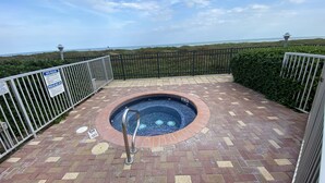 A spa area with a hot tub, surrounded by a brick patio and metal railings, overlooking a beach. -  Cozy Beach Condo Awaits on Padre Island! (South Padre Island)