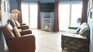 A living room with a ceiling fan, a TV, a bookshelf, and a sofa. -  Cozy Beach Condo Awaits on Padre Island! (South Padre Island)