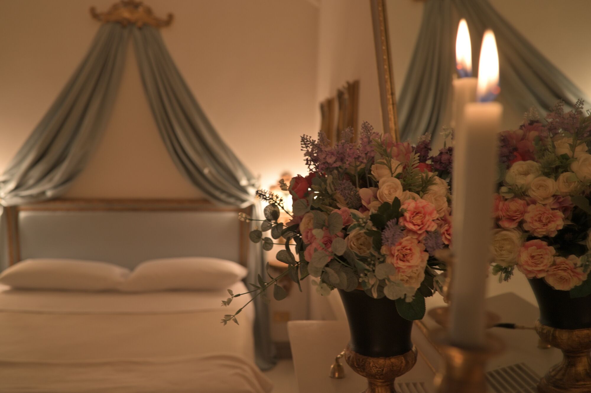 Ett sovrum med en himmelssäng, en vas med blommor och ett ljus.