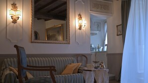 A cozy living room with a striped sofa, a wooden chair, a table with a lace tablecloth, and wall-mounted sconces. - At Handel's Refreshment House (Vignanello)