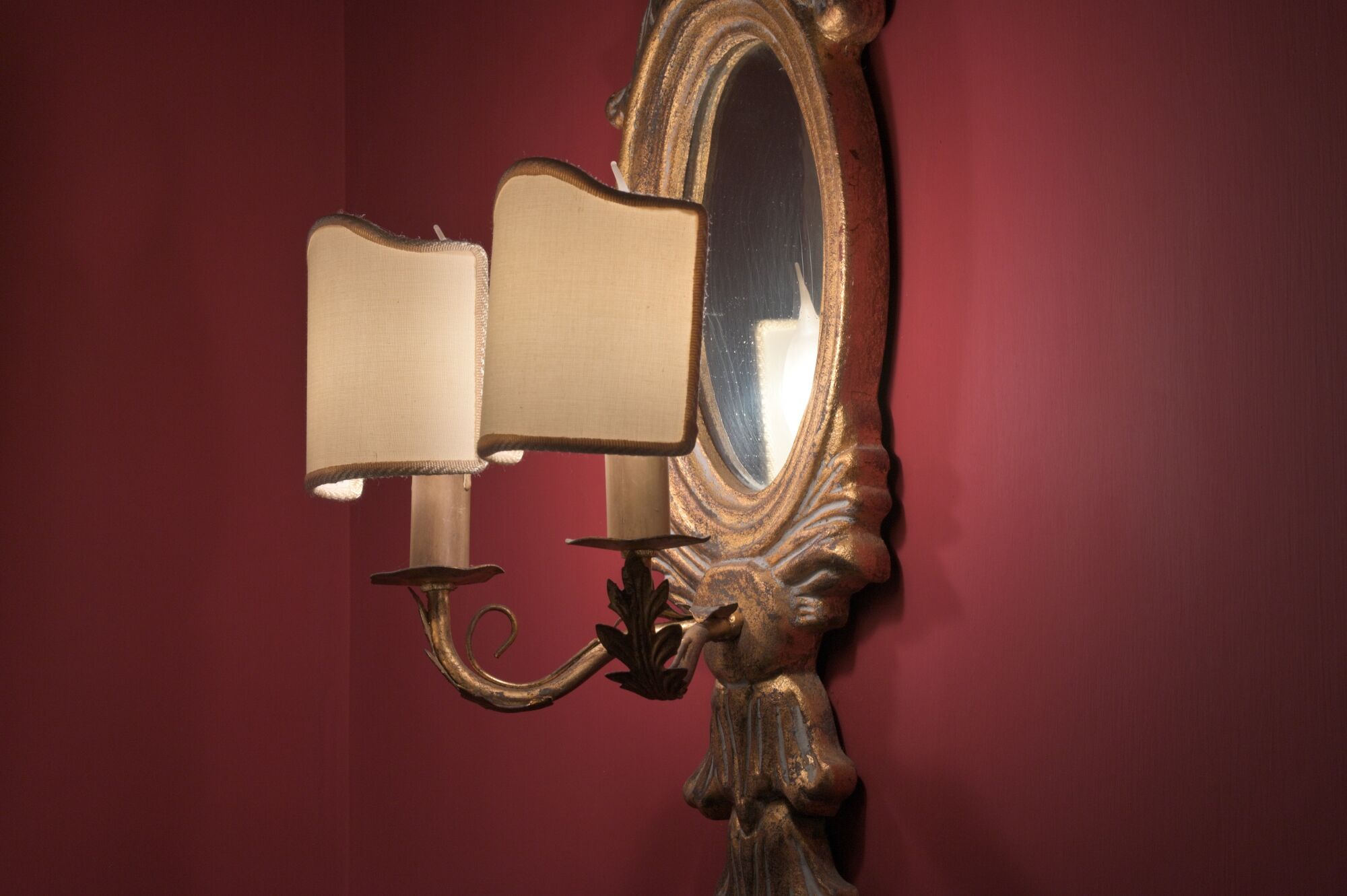Um espelho fixado na parede, com moldura decorada e duas luminárias.