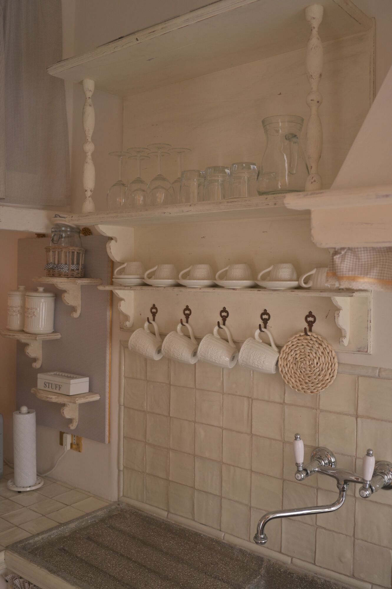 Une cuisine avec des carreaux blancs, un évier et divers ustensiles de cuisine blancs, notamment des tasses, des assiettes et des bocaux.