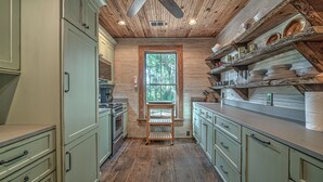 A kitchen with wooden cabinets, a stove, and a window with a view of trees.