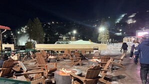 Ein Sitzbereich im Freien mit Stühlen und einer Feuerstelle, umgeben von einem Backsteinboden und Blick auf einen Berg.