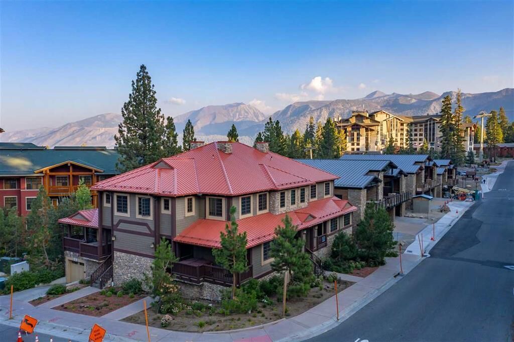 A multi-story building with a red roof, surrounded by trees and mountains in the background.