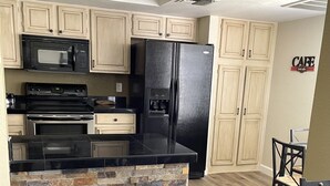 A modern kitchen with light wood cabinets, a black refrigerator, a microwave, and a stone accent wall. - Your Scottsdale Getaway awaits you with this wonderful poolside condo ! (Scottsdale)
