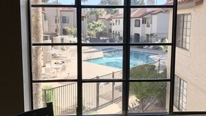 A view through a window with a pool and buildings in the background. - Your Scottsdale Getaway awaits you with this wonderful poolside condo ! (Scottsdale)