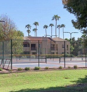 Residential building with a flat roof and balconies, surrounded by a secure fence and lush greenery.