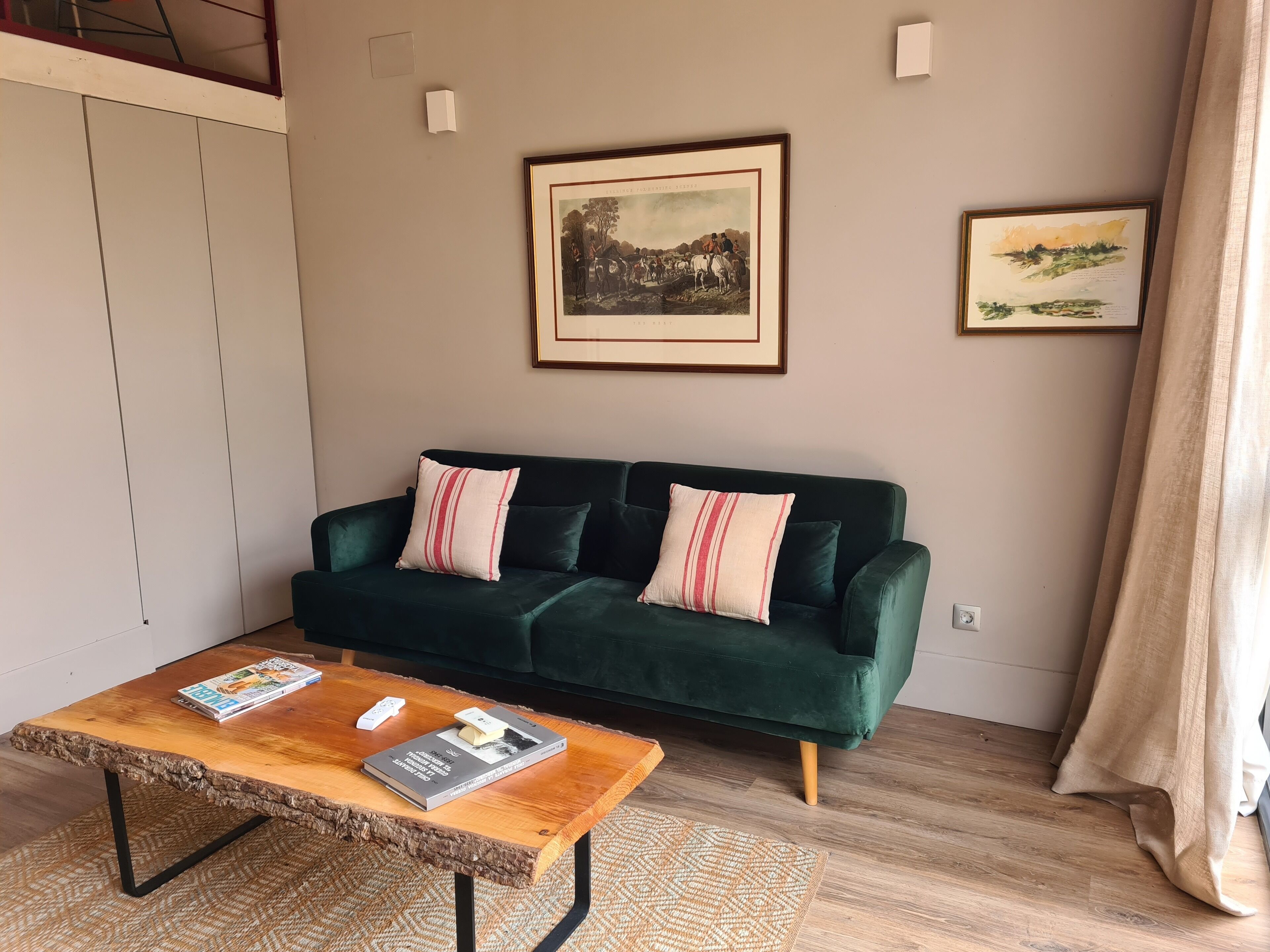 A living room with a green sofa, two pillows, a wooden coffee table with magazines, and two framed pictures on the wall.