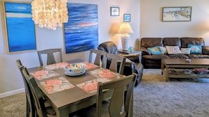 A dining area with a table set for four, a brown leather sofa, a coffee table, and a ceiling fan.