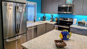 A modern kitchen with stainless steel appliances, a blue accent wall, and a unique hanging light fixture.