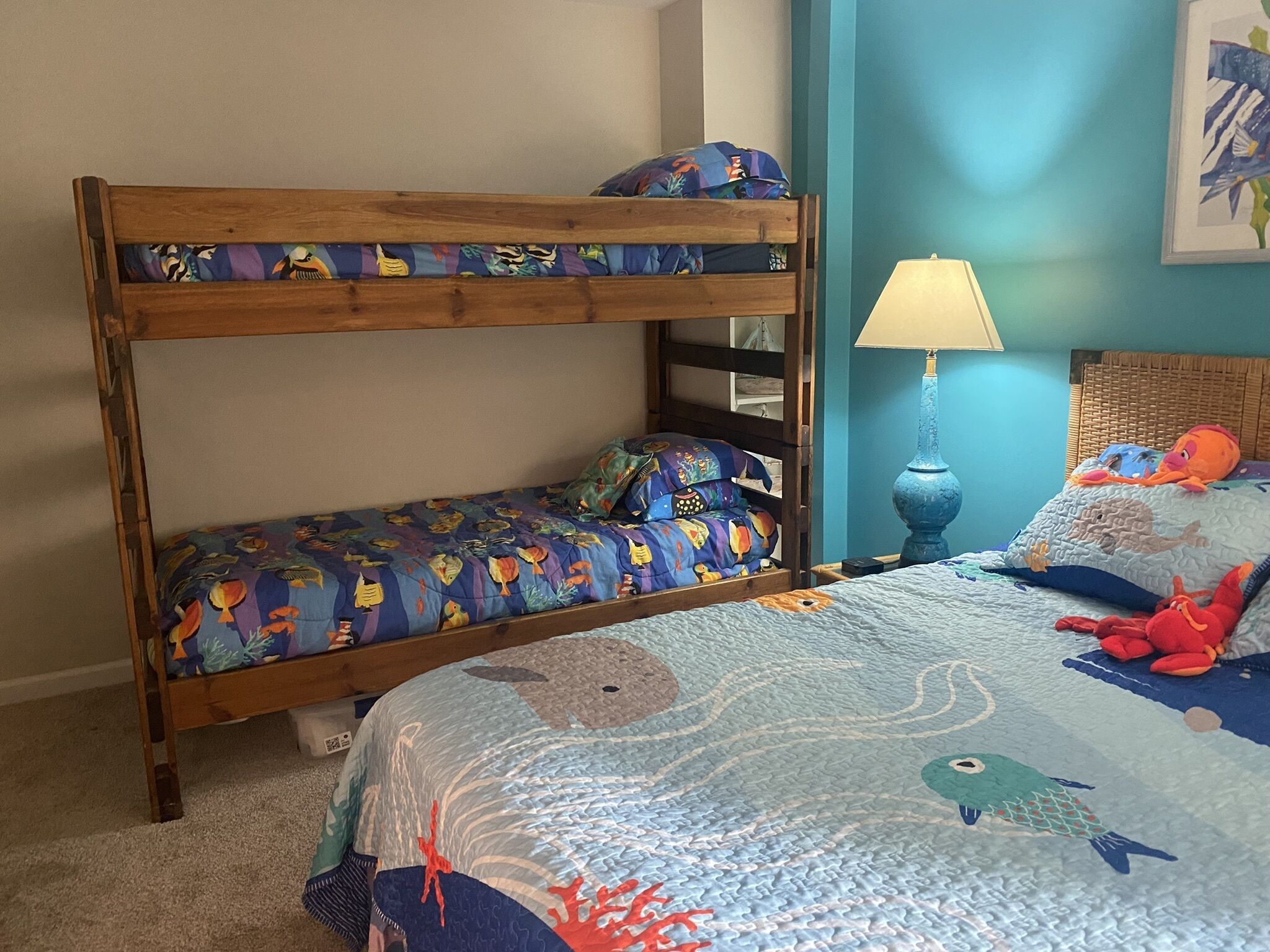 A bunk bed with a colorful fish-themed bedspread, a bedside lamp, and plush toys on the lower bunk.