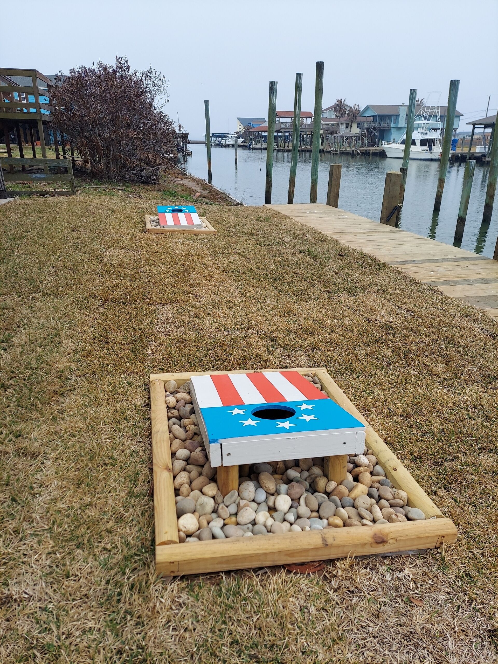 A wooden board game with a flag design on a grassy area near a dock with boats.